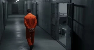 Homem caminhando por um corredor de prisão com as mãos agemas