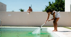 Foto de uma mulher limpando a piscina e vizinho ao fundo olhando