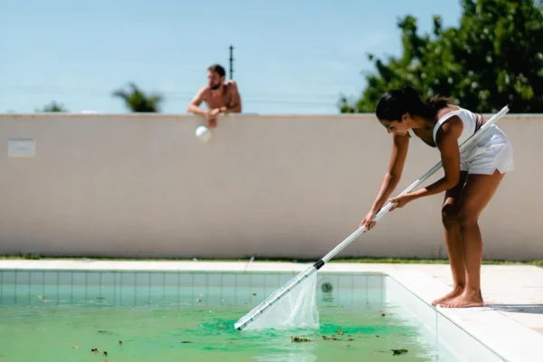 Foto de uma mulher limpando a piscina e vizinho ao fundo olhando